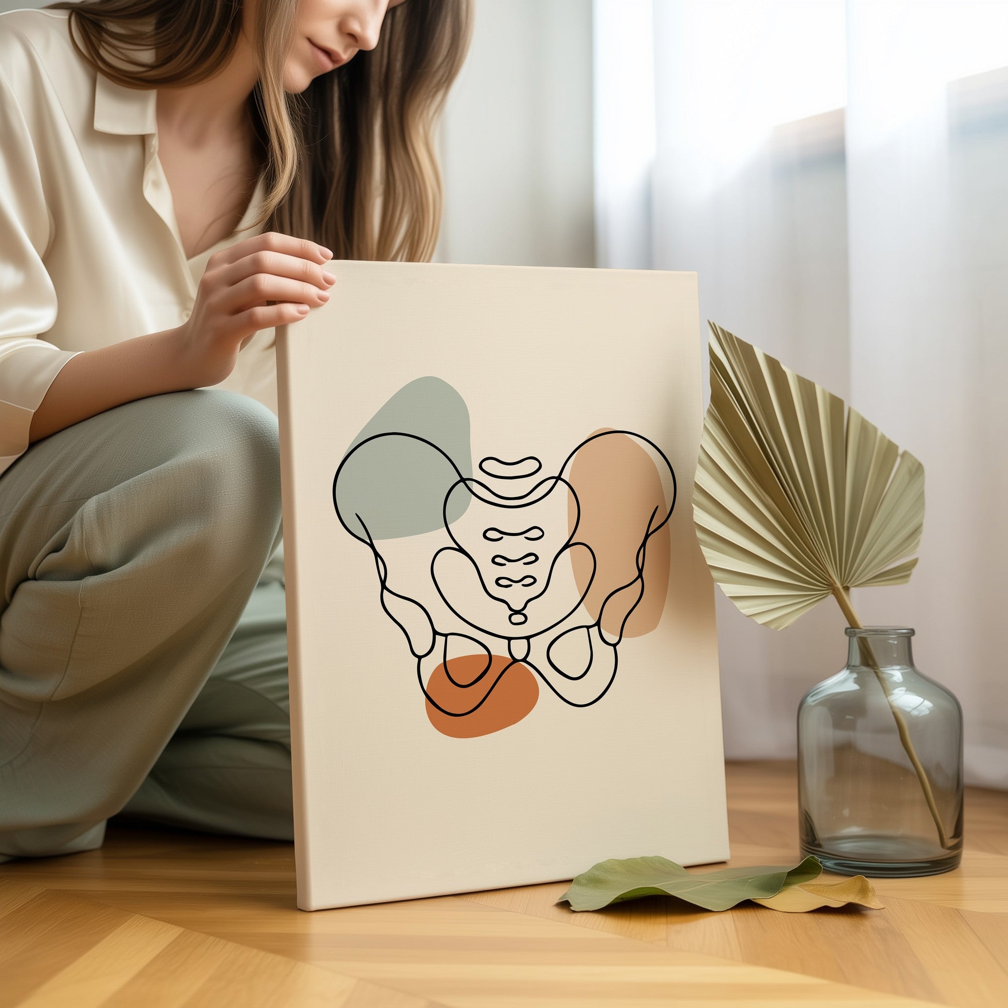 One line pelvis anatomy artwork held by a seated woman beside a vase and decorative leaves.