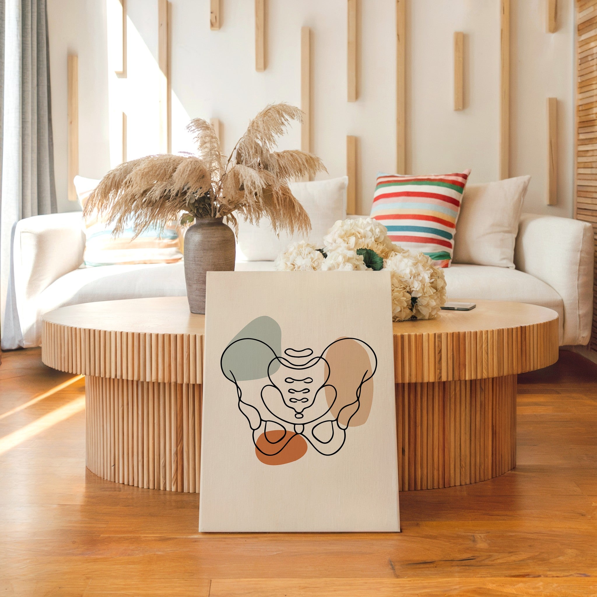 Pelvis anatomy canvas leaning in front of a round wooden coffee table in a bright living room.