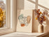 Pelvis line art canvas beside a vase of dried flowers on a sunny windowsill.