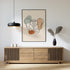 Black-framed pelvis line art displayed above a wooden sideboard with a pendant lamp and vase.