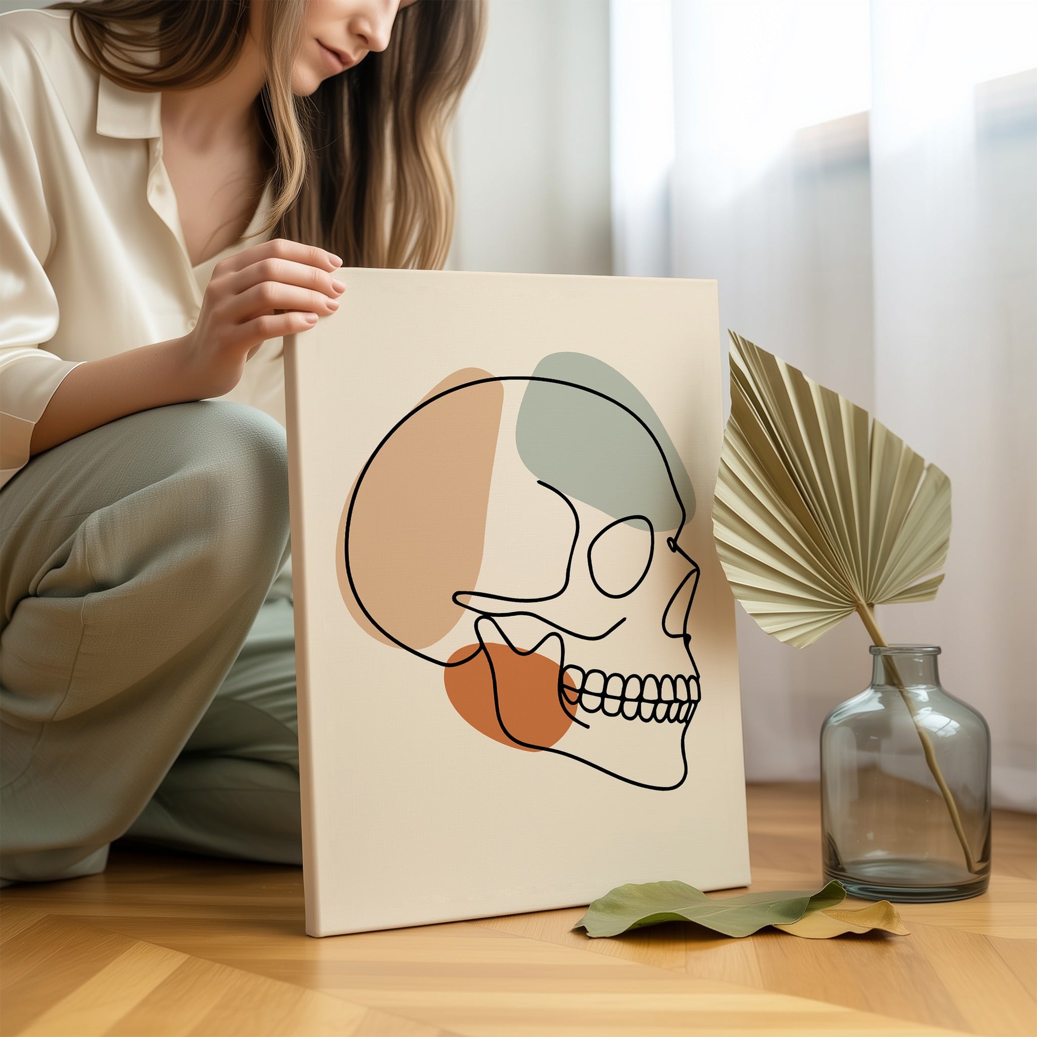Minimalist skull line art held by a person in a bright neutral room.