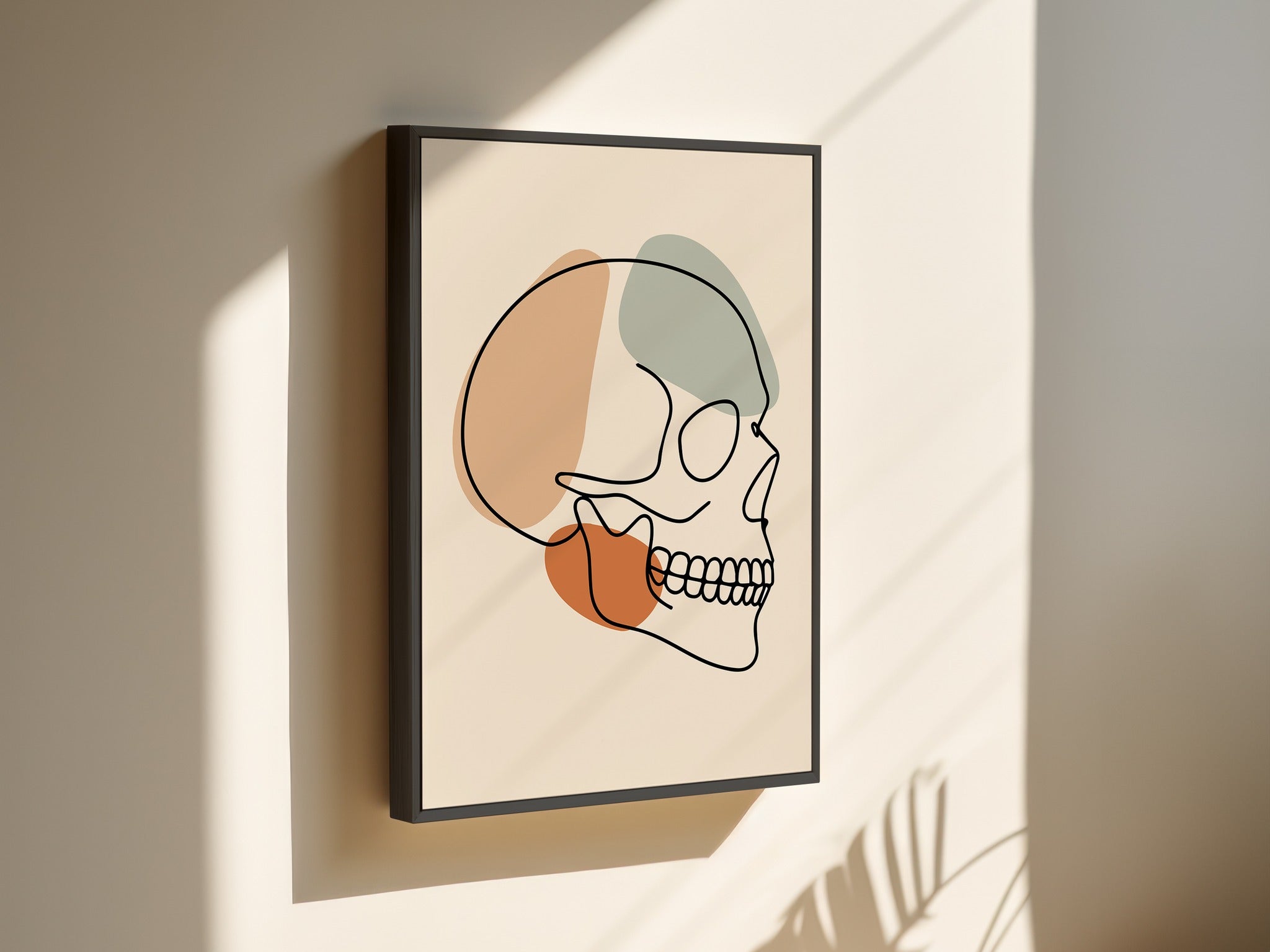 Minimalist skull line art on canvas in a black outer frame on a sunlit wall.