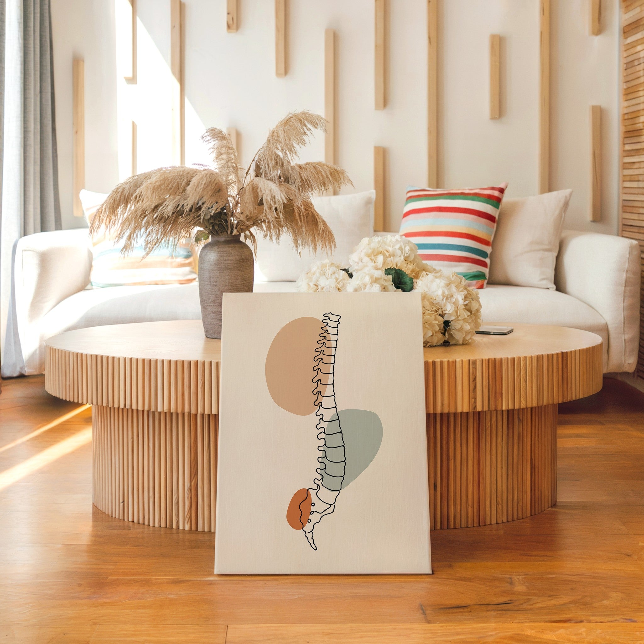 Spine anatomy canvas leaning in front of a round wooden coffee table in a bright living room.