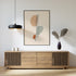 Black-framed spine line art above a wooden sideboard with a pendant lamp and vase.